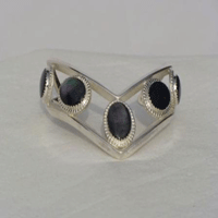 Five fouteen by ten millimeter oval Onyx stones bezel set connected by two triangular wires which are formed to a chevron shape. Worn with chevron pointing down